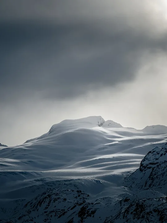 Des reliefs de neige ondulent sous un ciel sombre et une lumière diffuse.