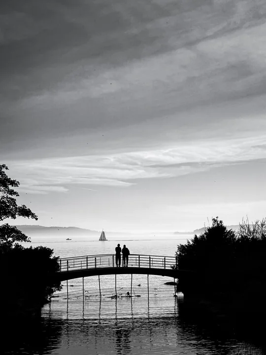 Deux silhouettes se tiennent sur une passerelle au-dessus de l’eau.