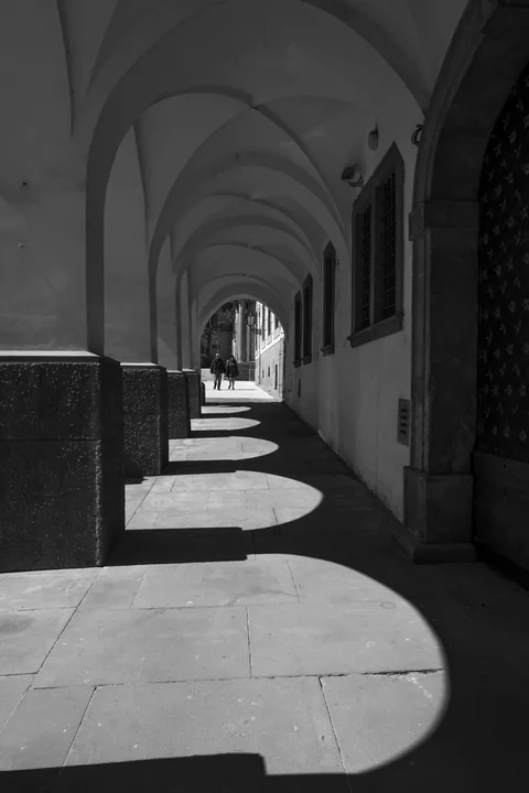 Une succession d’arcades projette des ombres courbes sur le sol.