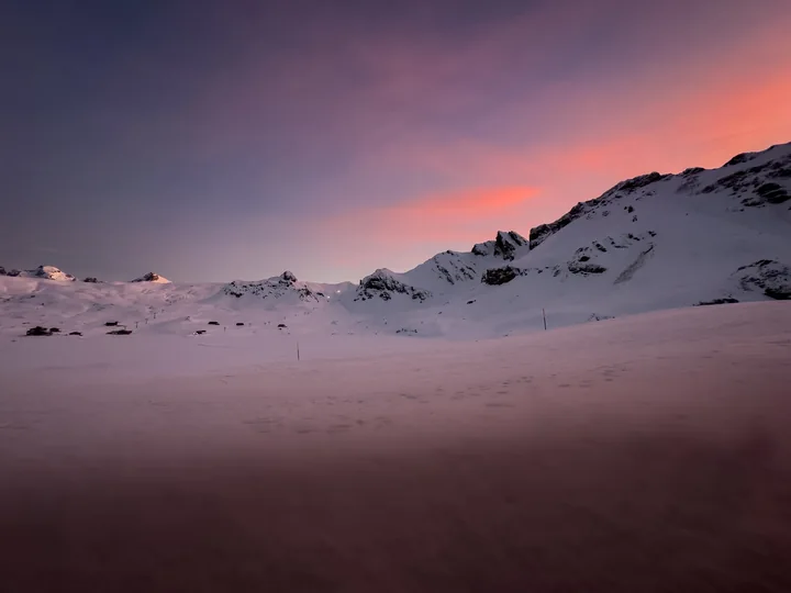 Une brume légère traverse un paysage enneigé sous un ciel rose.