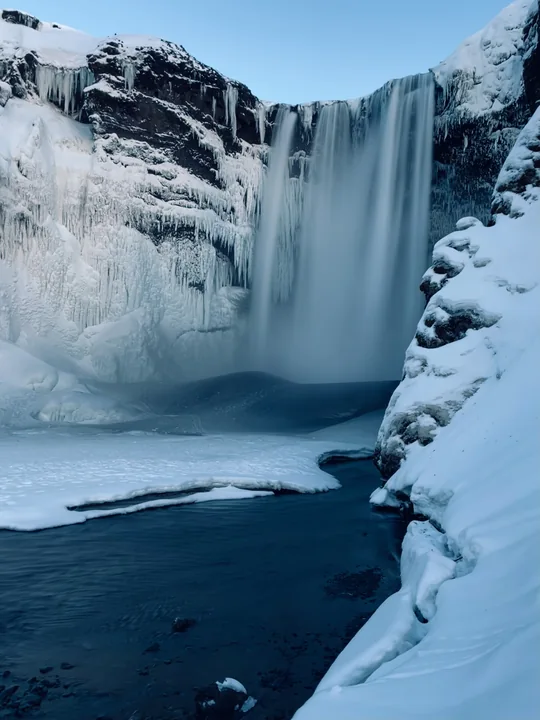 Une cascade coule entre des parois couvertes de glace et de neige.