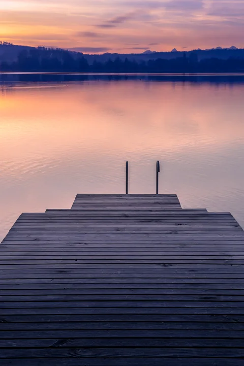 Un ponton vide avance vers un lac calme sous un ciel rose.
